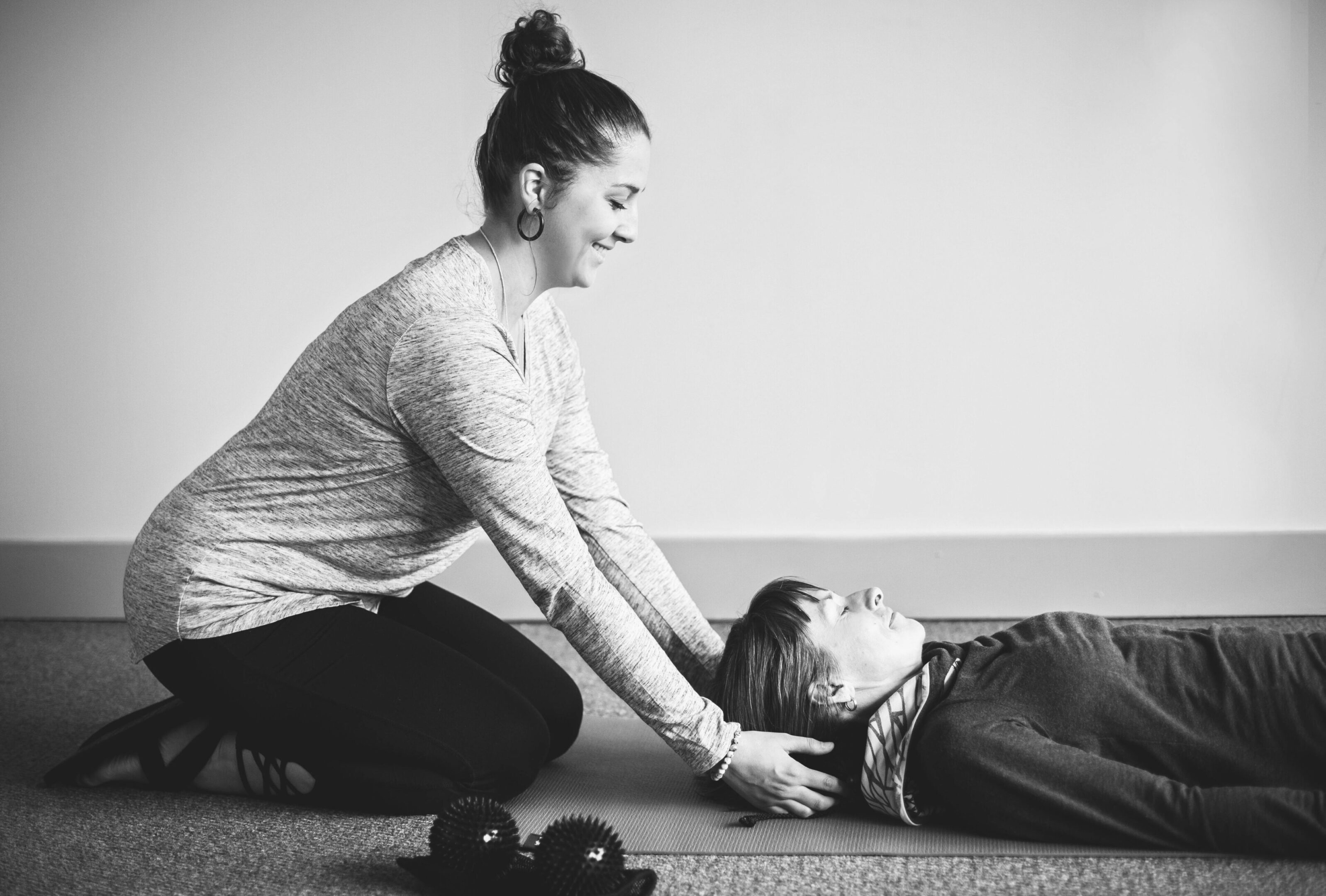 A woman helping another person stretch on the floor.