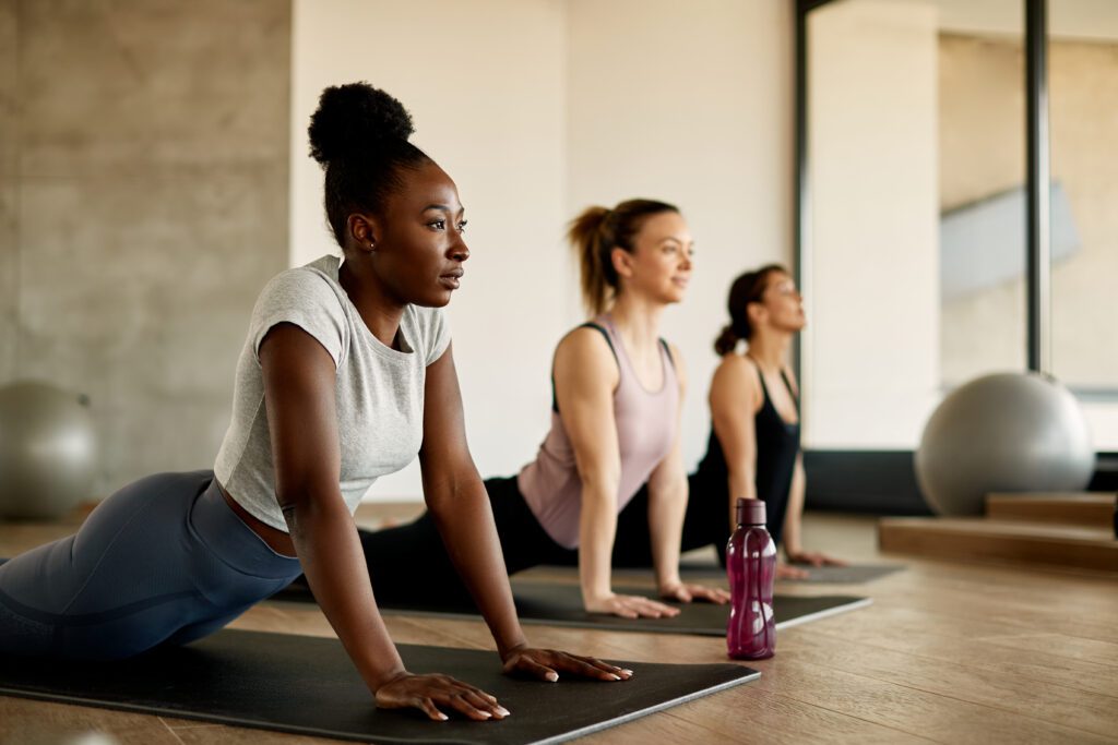Black female athlete doing stretching exercises while warming up with group of women at health club. A group of women doing yoga on mats.